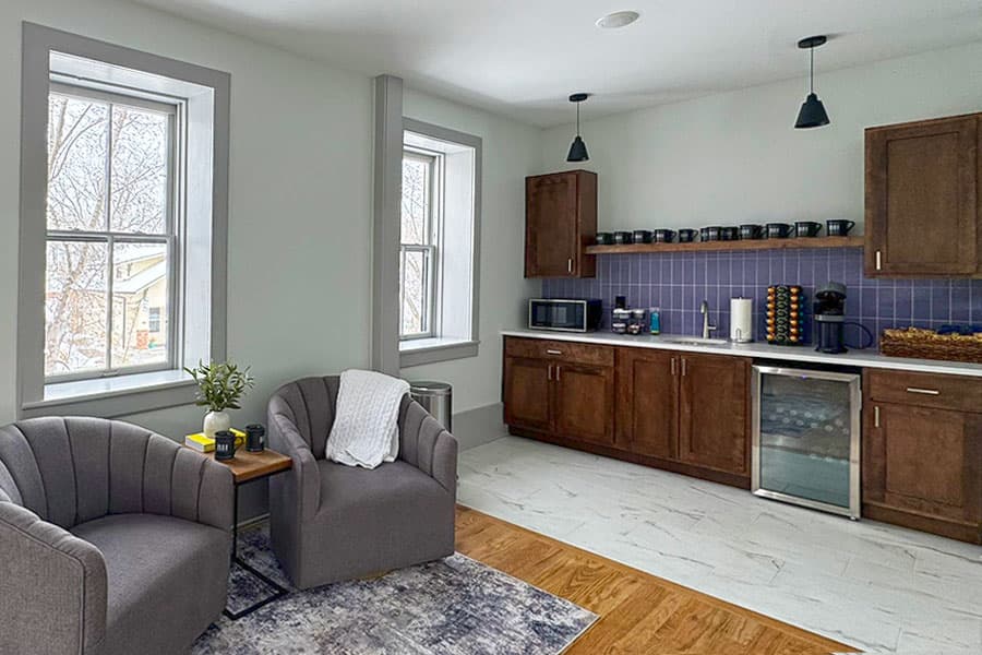 A modern kitchen featuring wooden cabinets, a coffee station, and comfortable seating by the windows.