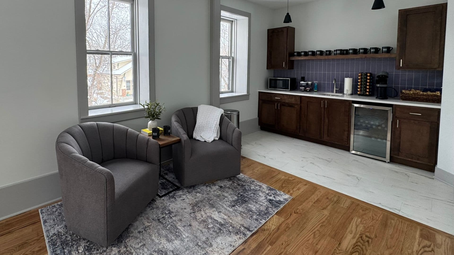 A cozy living area with two armchairs, a small table, and a modern kitchen in the background.