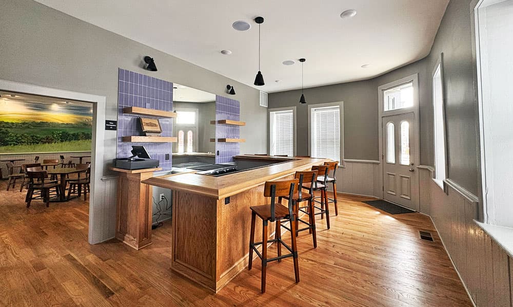 A modern kitchen with a wooden island, bar stools, and large windows, featuring a light color scheme and open layout.